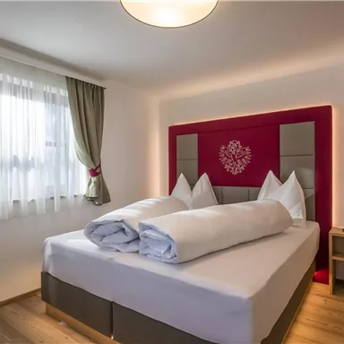 Ein gemütliches Schlafzimmer mit einem großen Bett und modernen Kissen. Große Fenster lassen viel Licht herein und die Wände sind in neutralen Farben gehalten.