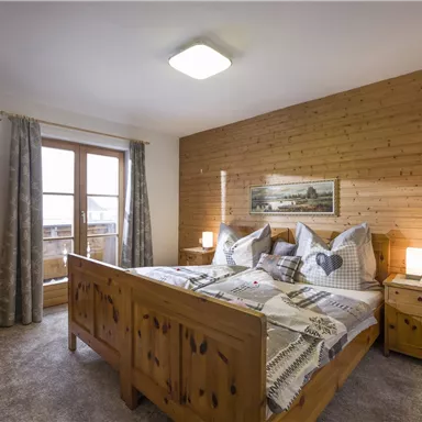A cozy bedroom with wooden furniture and a large bed. The walls are paneled with wood, and there is a window with a view.