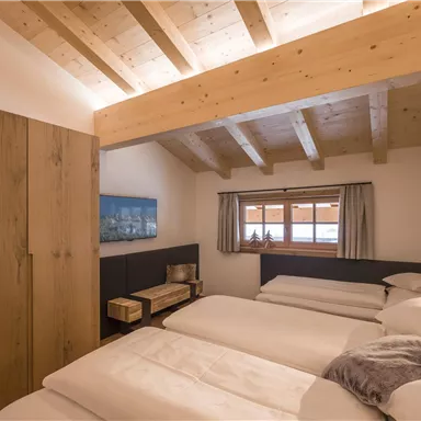 A cozy bedroom with wooden ceilings and three single beds. The decor is modern and offers a view from the window.