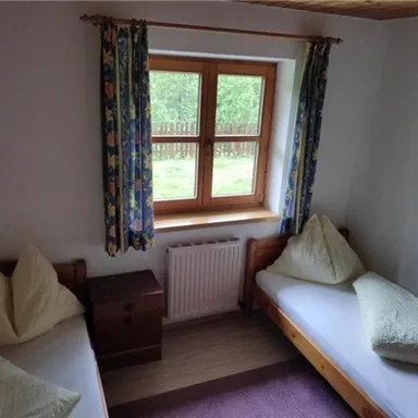 Ein einfaches Schlafzimmer mit zwei Betten und bunten Vorhängen. Der Raum hat ein Fenster mit Blick ins Freie.