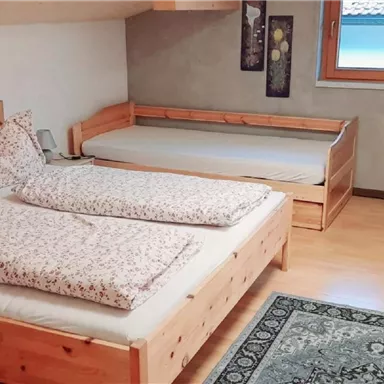 A cozy bedroom with two wooden beds and an additional sleeping space. The room is bright and feels inviting.