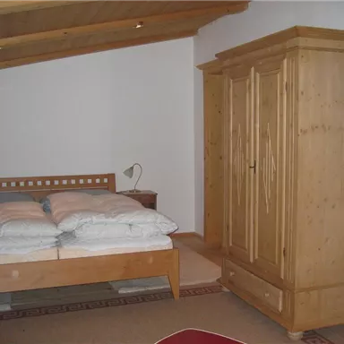 A cozy bedroom with a double bed and a wooden dresser. A television hangs on the wall and a bedside lamp stands next to the bed.