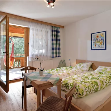 Ein gemütliches Schlafzimmer mit einem Doppelbett und Holzfußboden. Die Tür führt zu einem Balkon mit Blick ins Freie.