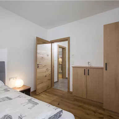 A modern bedroom with a double bed and wooden furniture. The door leads to an adjoining room.