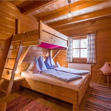 Ein gemütliches Holzschlafzimmer mit einem Etagenbett und zwei Betten. Das Zimmer hat helle Fenster und rustikale Einrichtung.