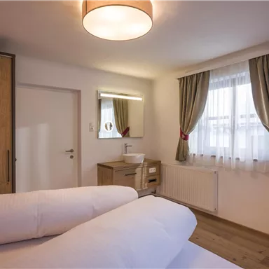 Ein gemütliches Zimmer mit zwei Betten, einem Holzschrank und einem großen Fenster. Die Wände sind hell, und es gibt einen modernen Fernseher an der Wand.