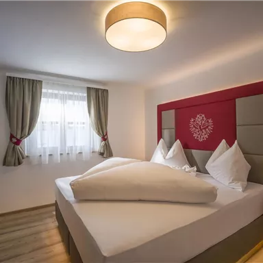 Ein modernes Schlafzimmer mit einem großen Doppelbett und gemütlicher Einrichtung. Die Fenster sind mit Vorhängen versehen und es gibt sanfte Beleuchtung.