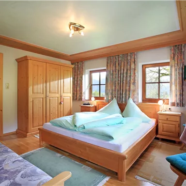 Ein gemütliches Schlafzimmer mit Holzmöbeln und zwei Fenstern. Das Bett hat grüne Decken und es gibt einen kleinen Tisch mit einem Stuhl.