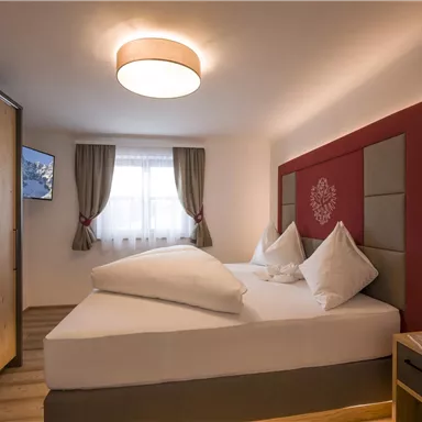 Ein modernes Zimmer mit zwei Einzelbetten und hellen Vorhängen. Der Raum ist gemütlich eingerichtet und bietet einen Fernseher sowie einen Nachttisch.