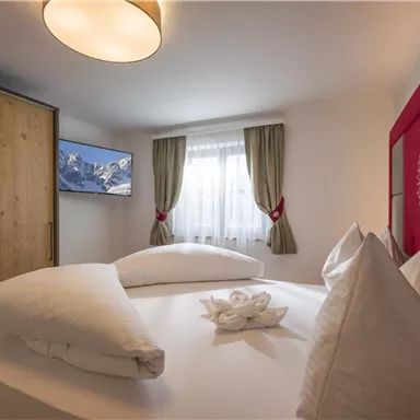 Ein gemütliches Schlafzimmer mit einem großen Bett und dekorativen Kissen. Das Zimmer verfügt über einen Fernseher und einen Holzschrank.