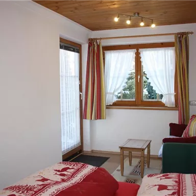 Ein gemütliches Zimmer mit einem Fenster, das viel Licht hereinlässt. Farbig gestreifte Vorhänge und eine kleine Sitzecke sorgen für eine einladende Atmosphäre.