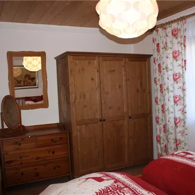 Ein gemütliches Schlafzimmer mit Holzmöbeln und einer Blumendekoration. Ein großer Kleiderschrank und ein Spiegel ergänzen den Raum.