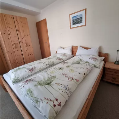 Ein gemütliches Schlafzimmer mit einem Doppelbett und frischen Bettdecken. Der Raum besitzt einen Kleiderschrank aus Holz und ein Bild an der Wand.