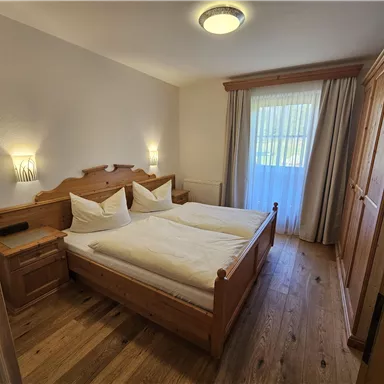 Ein gemütliches Schlafzimmer mit zwei Betten und Holz-Möbeln. Das Zimmer ist hell und einladend, mit einem Fenster, das Tageslicht hereinlässt.