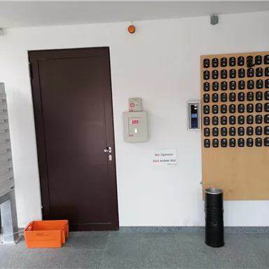 An entrance area with mailboxes on the left side and a dark door. On the wall are many key boxes and an intercom device.