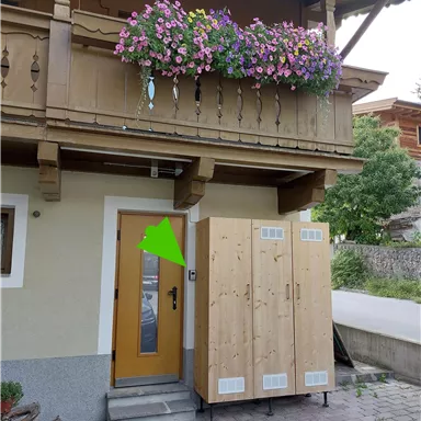 Ein gemütliches Holzhaus mit einem blühenden Balkon. Vor der Tür steht ein großer, hölzerner Schrank.