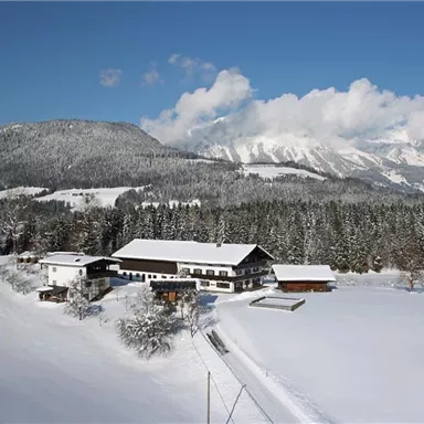 A winter landscape with snow-covered fields and mountains. A cozy house stands in the middle of the scene.