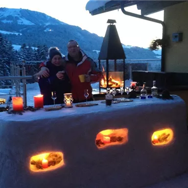 A cozy outdoor area with a snow bar and atmospheric lighting. Two people are standing together, enjoying the winter atmosphere in the mountains.
