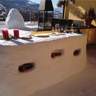Ein schneeweißer Tisch aus Schnee auf einer Terrasse in den Bergen. Auf dem Tisch stehen Getränke und weihnachtliche Dekoration.