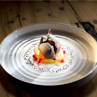 Ein kunstvoll angerichtetes Dessert auf einem weißen Teller. Es besteht aus Schokoladeneis, orangefarbenem Fruchtpüree und roten Beeren.