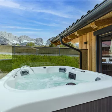 Ein Whirlwanne steht an einem modernen Haus mit Blick auf die Berge. Die Umgebung ist grün und die Atmosphäre ruhig und entspannend.