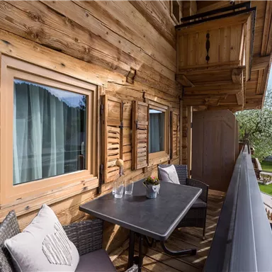 Ein gemütlicher Balkon mit Holzverkleidung und einem Tisch mit Stühlen. Im Hintergrund ist ein grüner Garten zu sehen.