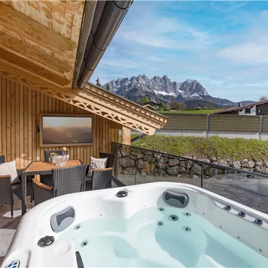 Ein moderner Whirlpool auf einer Terrasse mit Blick auf die Berge. Die Holzverkleidung und der Himmel verleihen der Umgebung eine gemütliche Atmosphäre.