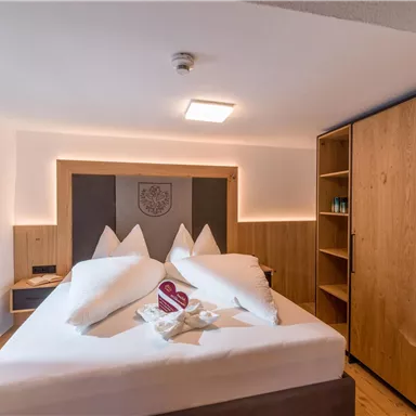 Ein modernes Hotelzimmer mit einem großen Doppelbett und Holzdetails. Die Einrichtung ist hell und einladend, mit einem Fenster und einem Kleiderschrank.