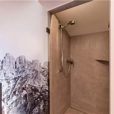 Eine moderne Dusche mit Fliesen in neutralen Farben. Im Hintergrund ist ein Bergmotiv an der Wand zu sehen.