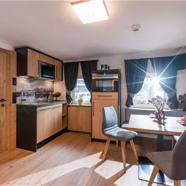 Eine moderne Küche mit Holzschränken und einem kleinen Esstisch. Das Licht fällt durch ein Fenster und verleiht dem Raum eine freundliche Atmosphäre.