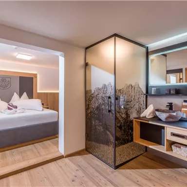 Ein modernes Zimmer mit einem bequemen Bett und eleganten Holzelementen. Das Badezimmer ist durch eine stilvolle Glaswand abgetrennt.