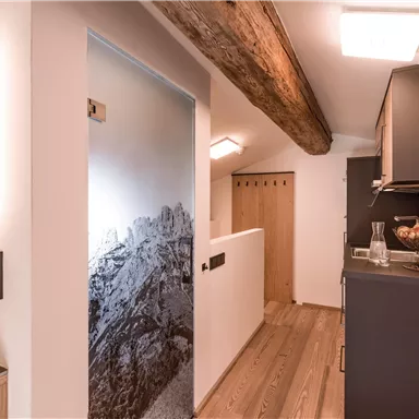 Ein moderner Flur mit Holzfußboden und einer eleganten Küche. Die Wände sind hell und es gibt eine interessante grafikartige Tür mit Bergmotiven.