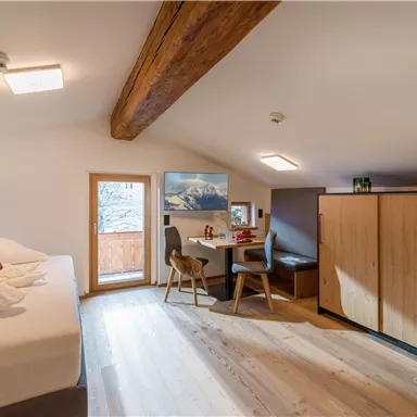 Ein gemütliches Zimmer mit einem großen Bett, einem Tisch und Stühlen. Es hat Fenster mit Blick auf die Berge und einen warmen Holzfußboden.