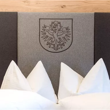 Ein elegantes Kopfteil mit einem Wappen und dekorativen Kissen. Die Farbgestaltung ist schlicht und modern.