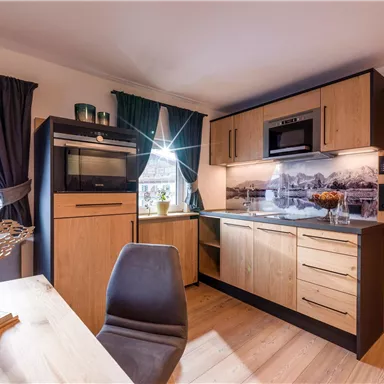 Eine moderne Küche mit Holzschränken und einer eleganten Arbeitsfläche. Der Raum ist hell und gut eingerichtet mit einem Tisch und Stühlen.