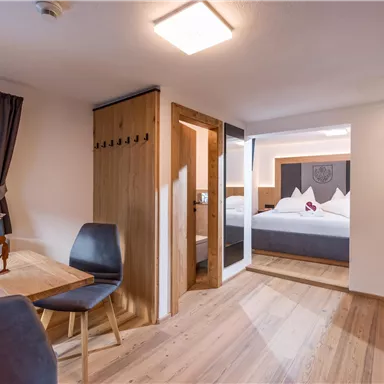 Ein modernes Zimmer mit Holzfußboden und gemütlicher Einrichtung. Es gibt einen Essbereich, einen Kleiderschrank und ein angrenzendes Schlafzimmer.