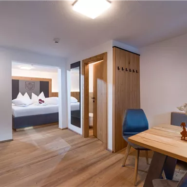 Ein modernes Hotelzimmer mit Holzboden und eleganten Möbeln. Es gibt einen Essbereich und eine Verbindung zu einem weiteren Schlafzimmer.