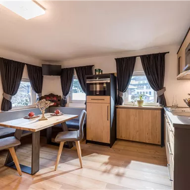 Eine gemütliche Küche mit einem Esstisch und modernen Möbeln. Große Fenster lassen viel Licht herein und der Raum wirkt einladend.