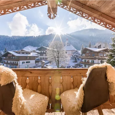 Eine gemütliche Veranda mit zwei Stühlen und Blick auf schneebedeckte Berge. Die Sonne scheint hell in die Winterlandschaft.