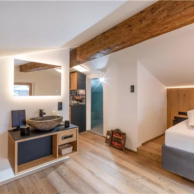 Ein modernes Schlafzimmer mit einem großen Bett und Holzdecken. Ein stilvoller Waschbereich mit einem großen Spiegel und einem gemütlichen Ambiente.