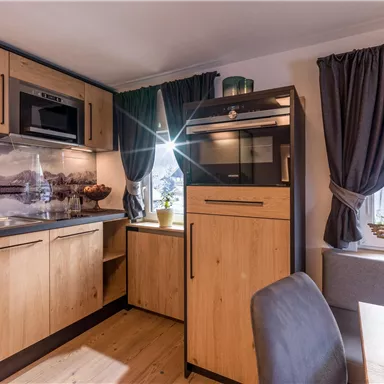 Eine moderne Küche mit Holzschränken und eingebauten Geräten. Große Fenster sorgen für helles Licht und eine gemütliche Atmosphäre.