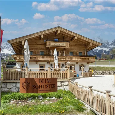 Ein traditionelles Holzhaus in den Alpen mit einem gemütlichen Außenbereich. Umgeben von prächtigen Bergen und grünem Gras.
