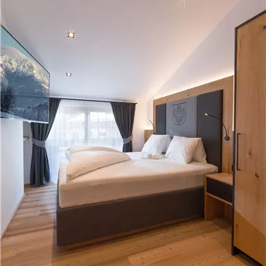 Ein modernes Schlafzimmer mit zwei Einzelbetten und einem großen Fernseher. Große Fenster sorgen für viel Tageslicht und eine angenehme Atmosphäre.