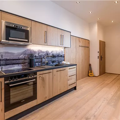 Eine moderne Küche mit Holzschränken und einer eleganten Arbeitsfläche. Der Raum ist hell und einladend, mit einer großen Fensterfläche und warmem Licht.