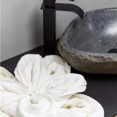 Ein stilvolles Badezimmer mit einem eleganten Waschbecken aus Stein und einem modernen Wasserhahn. Ein fein gefaltetes Handtuch liegt auf der Ablage.