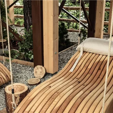 Eine gemütliche Holzliege mit einem Kissen in einem modernen Bereich. Umgeben von Natur und Holzstruktur.