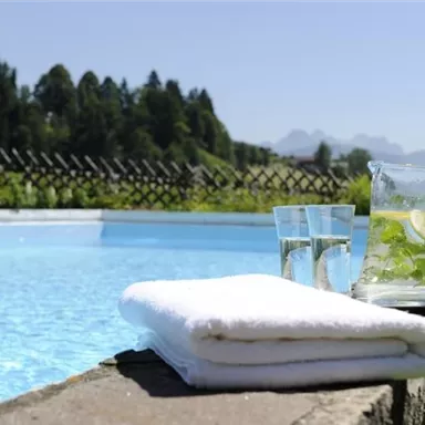 Ein erfrischender Pool mit klarem Wasser und einem Handtuch daneben. Auf dem Rand stehen eine Karaffe mit Getränk und Gläser.