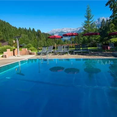 Ein Pool in einer schönen Landschaft mit Bergen im Hintergrund. Liegen und Sonnenschirme laden zum Entspannen ein.