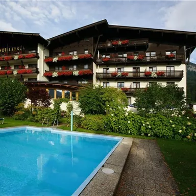 Ein malerisches Hotel mit großzügigen Balkonen, die mit Blumen geschmückt sind. Neben dem Hotel befindet sich ein einladender Pool in einer grünen Gartenlandschaft.