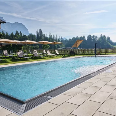 Ein erfrischender Pool mit klarem Wasser und einem Handtuch daneben. Auf dem Rand stehen eine Karaffe mit Getränk und Gläser.